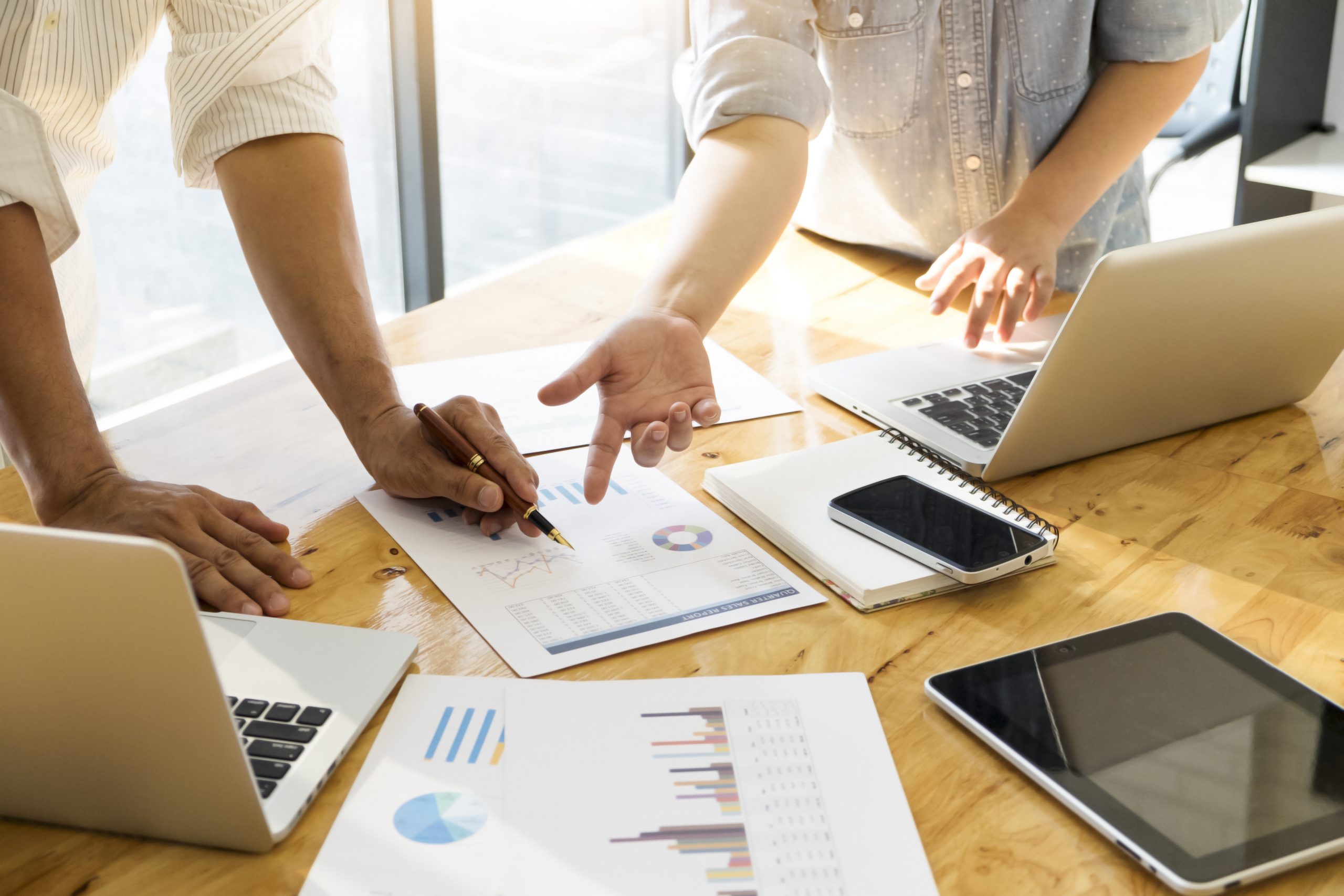 FMEA: o que é, como aplicar e quais as suas vantagens? | Na imagem aparece apenas as mãos de pessoas sobre uma mesa apontando para alguns papéis e notebook.